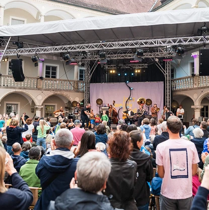 Über das Publikum hinweg sieht man eine Bühne mit einer erwachsenen Band und drei Kindern.